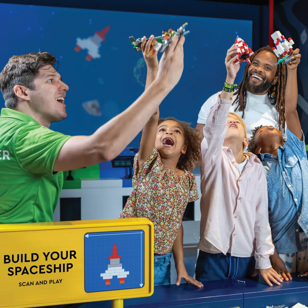 A master model builder at LEGO Discovery Center Atlanta is helping a dad and his three kids build a spaceship as part of the 